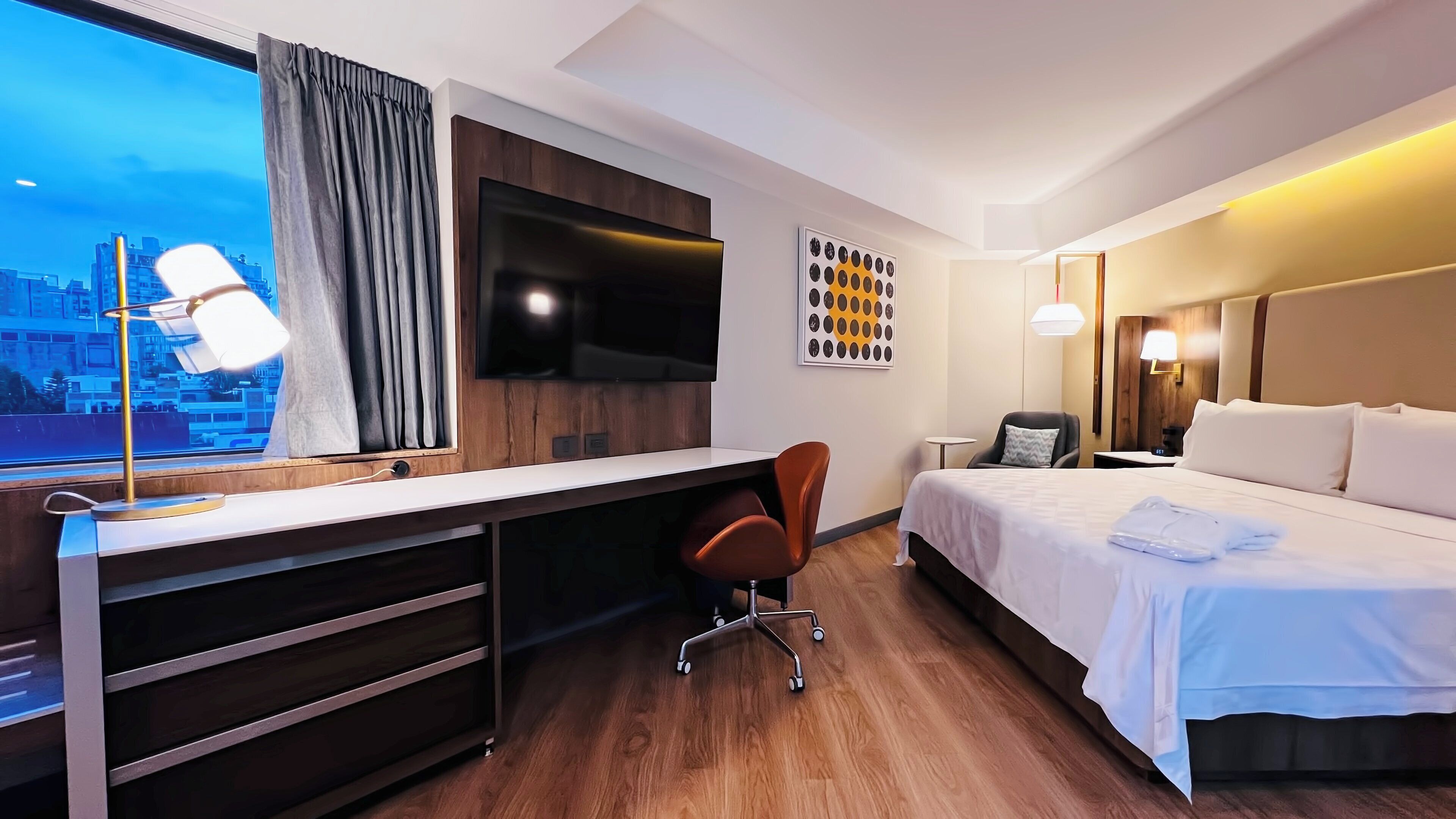 Una habitación de hotel con escritorio, silla, cama y televisor montado en la pared.