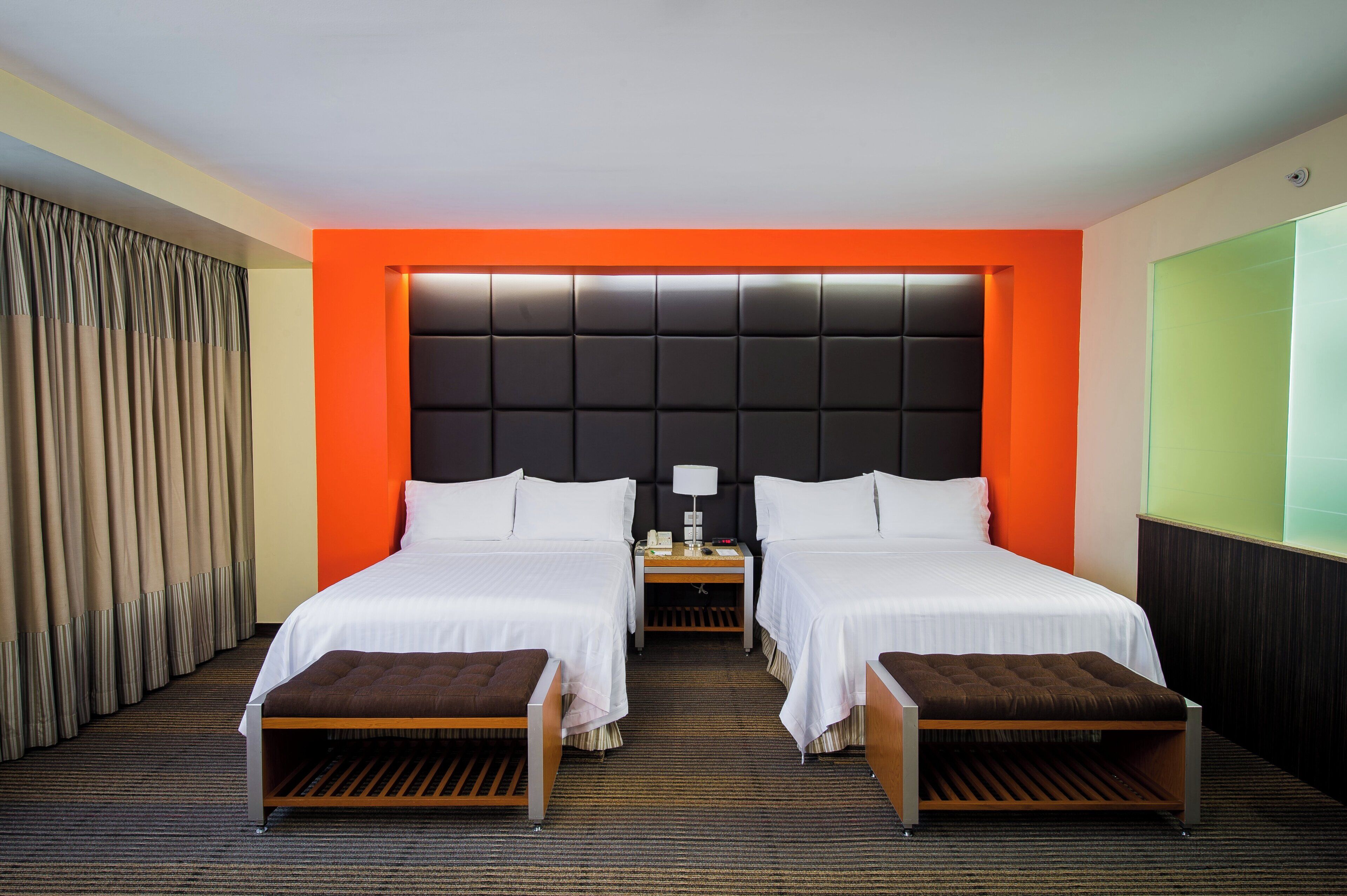 Une chambre d’hôtel avec deux lits, une table de chevet, une lampe et une grande fenêtre.