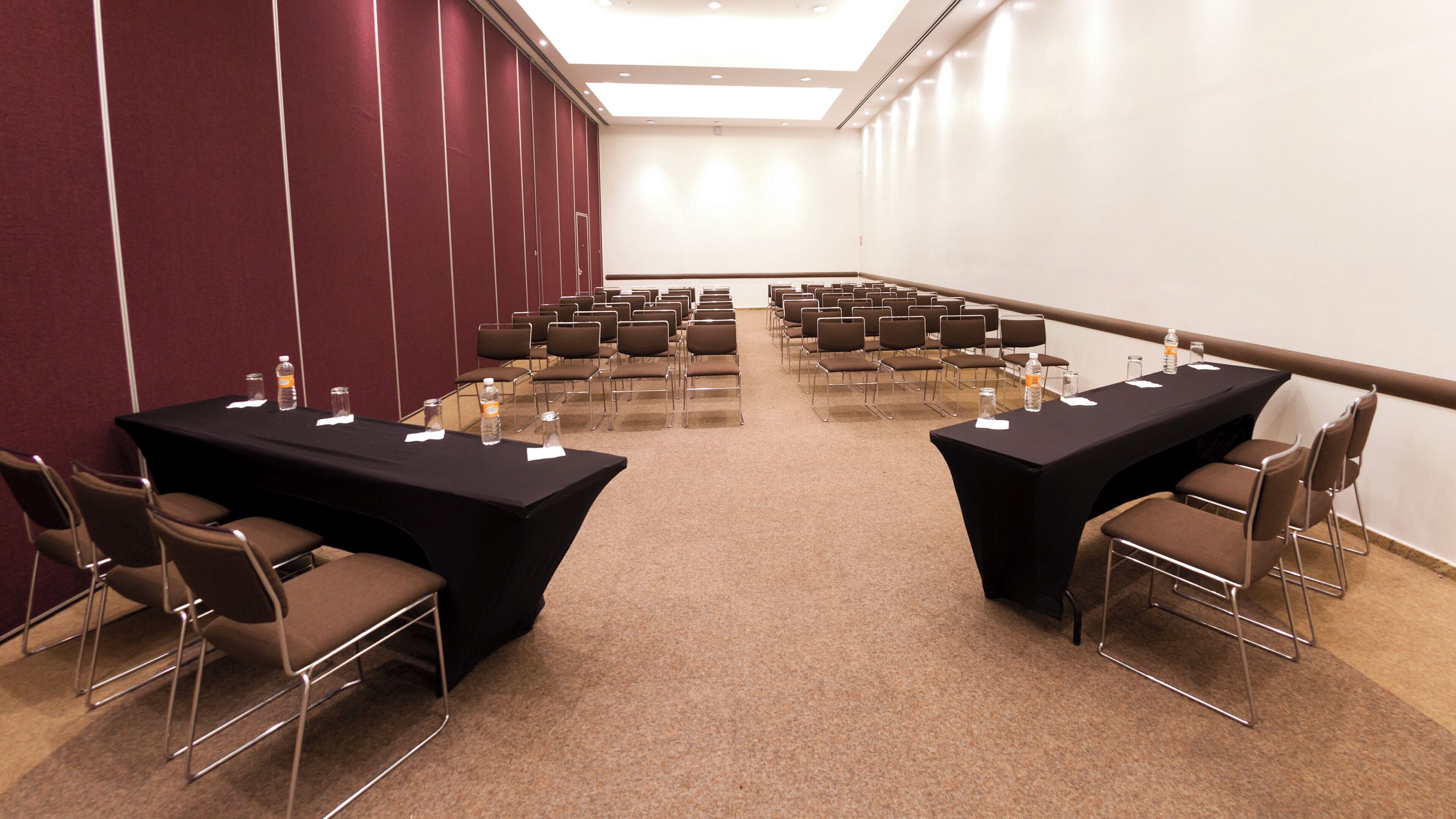 A conference room with two long tables, chairs, and water bottles.