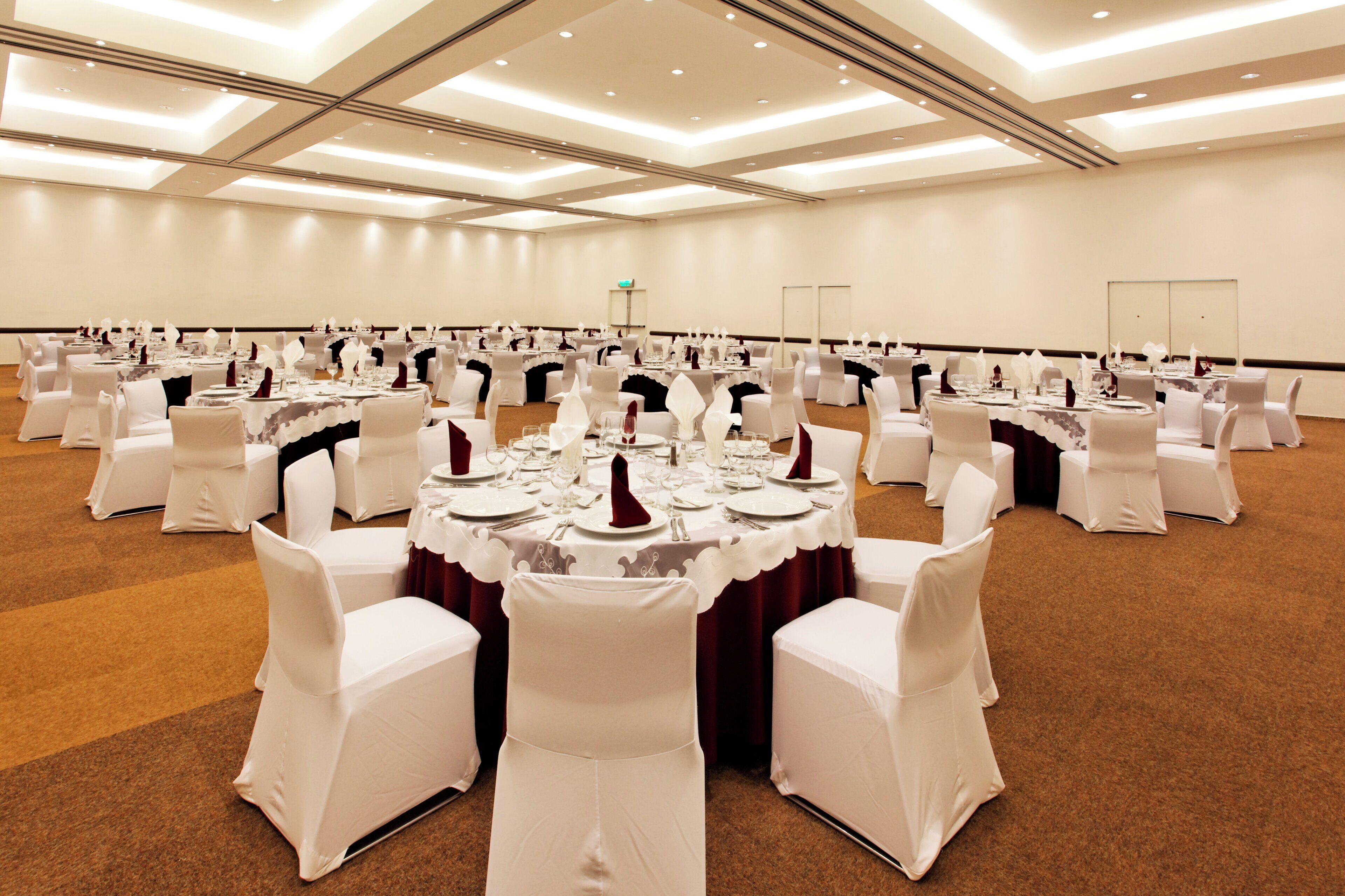 A large banquet hall with round tables set for dining, white chairs, and a carpeted floor.