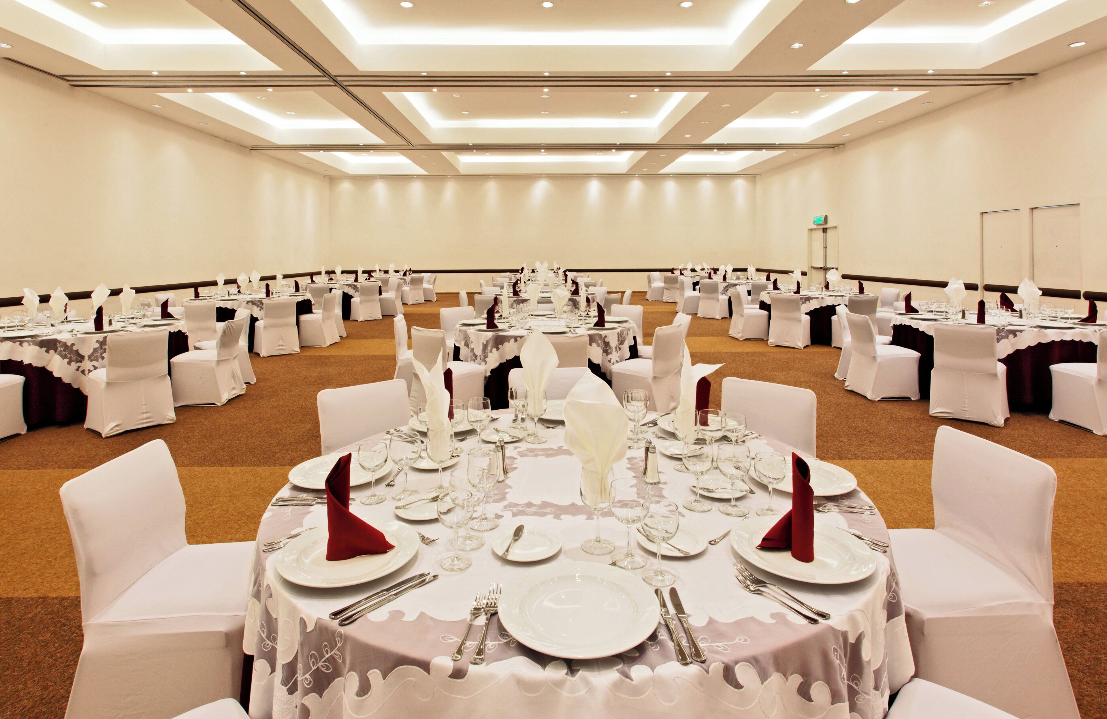 Un salón de banquetes con mesas redondas dispuestas para un evento formal, con manteles blancos, cubiertos y cristalería.