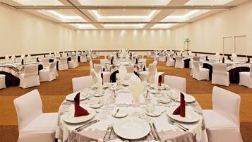 Un salón de banquetes con mesas redondas dispuestas para un evento formal, con manteles blancos, cubiertos y cristalería.
