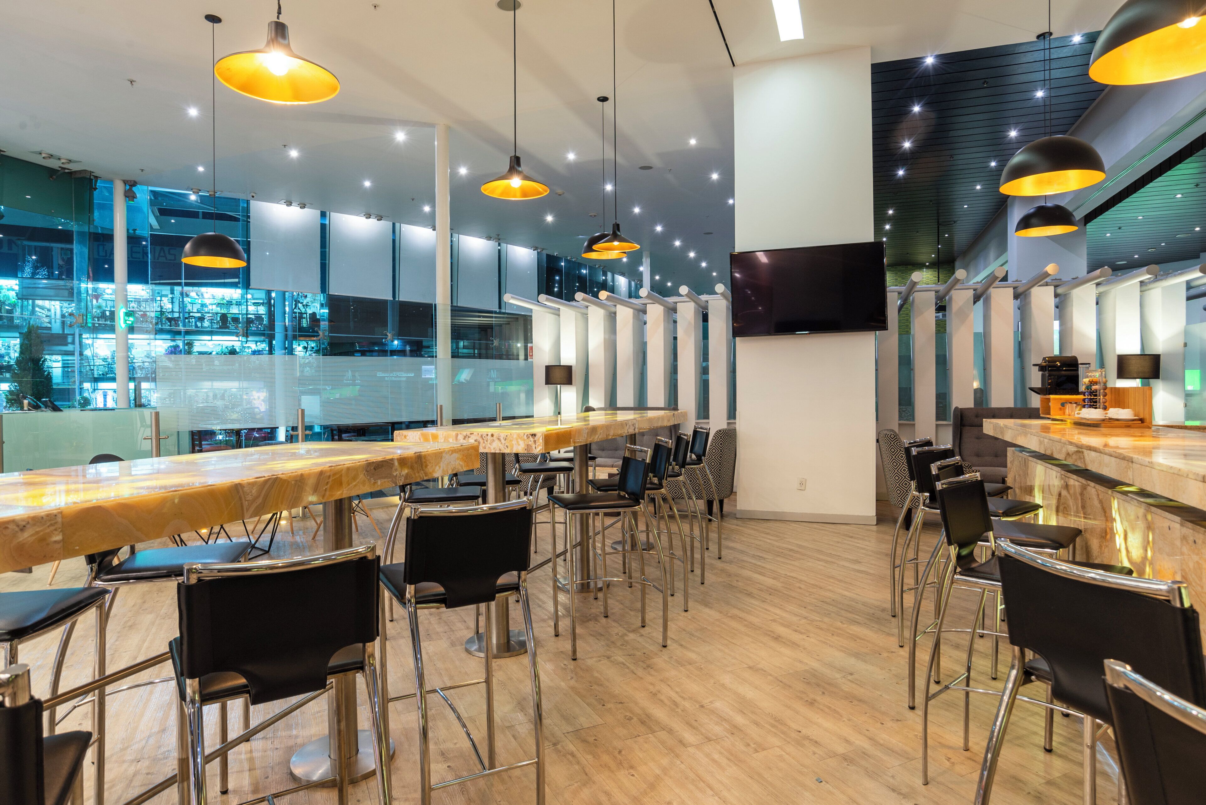 Un espacio de bar moderno con una barra larga, varios taburetes y lámparas colgantes.