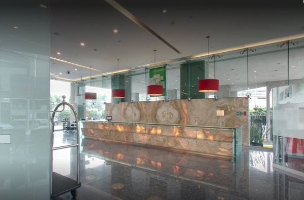 Un vestíbulo moderno con mostrador de recepción de mármol, paredes de vidrio e iluminación colgante roja.