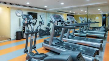 Un gimnasio con varias cintas de correr, elípticas y un espejo grande.