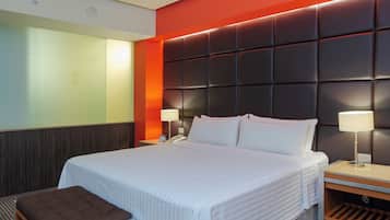 A hotel room with a large bed, bedside lamps, a wooden bench, and a modern headboard.