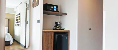 Una kitchenette compacta equipada con microondas, cafetera y refrigerador pequeño.