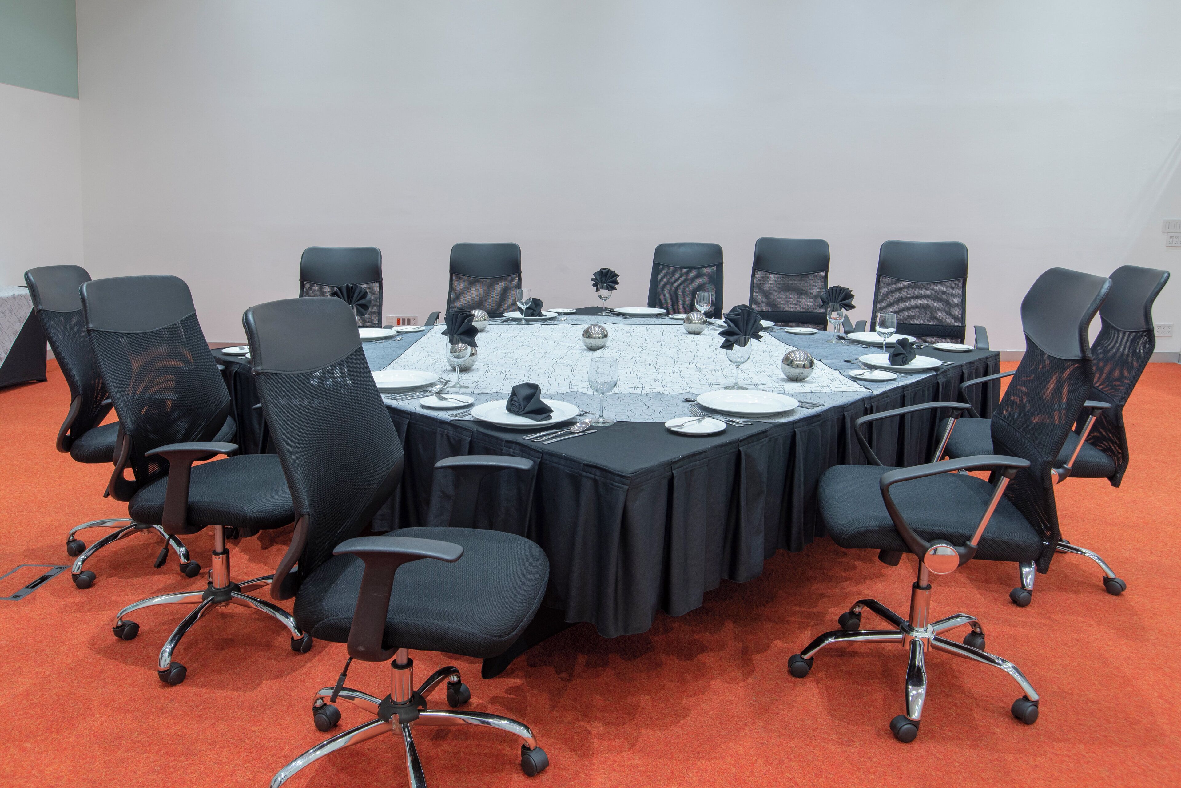 Ein Konferenzraum mit rundem Tisch, schwarzen Stühlen und einer weißen Tischdecke.