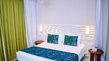 Une chambre d’hôtel avec un lit, deux tables de chevet, un ventilateur de plafond et une petite table de nuit avec un téléphone.