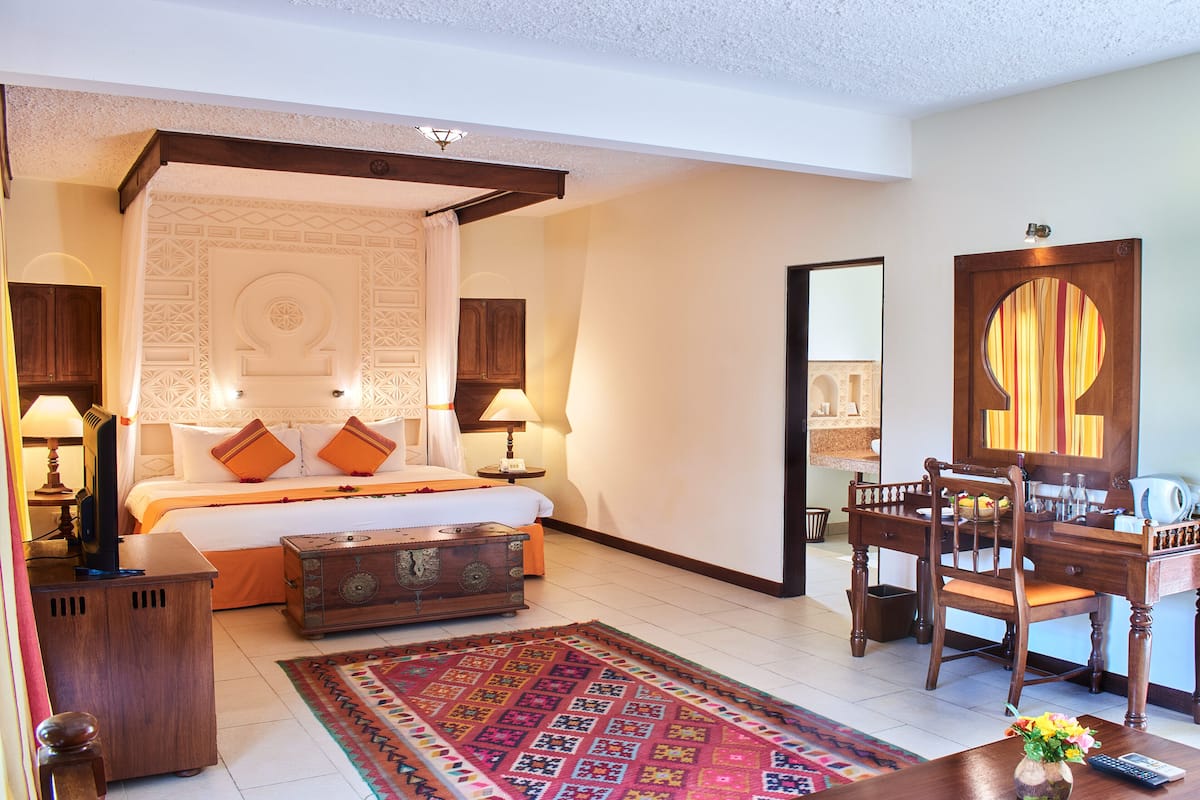 A bedroom with a four-poster bed, bedside tables, a wooden desk, and a chair.
