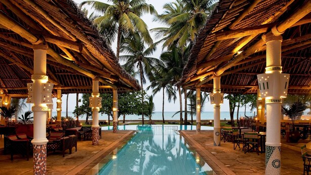 Un área junto a la piscina con vista despejada al océano, palmeras y una estructura de techo de paja.