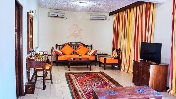 A living room with a sofa, chairs, a coffee table, a television, and a patterned rug. - Neptune Village Beach Resort & Spa All Inclusive (Diani Beach)