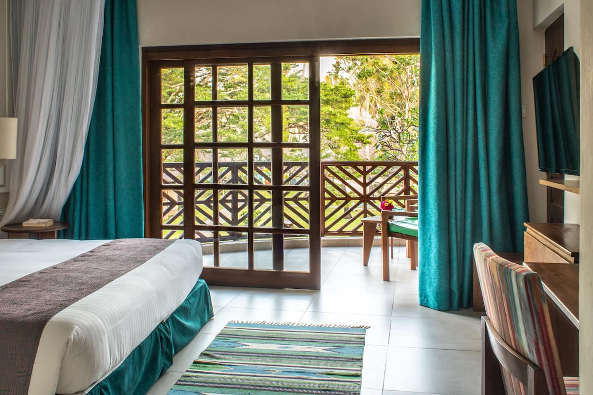 A hotel room with a bed, a wooden chair, a TV, and a view of the outdoors.