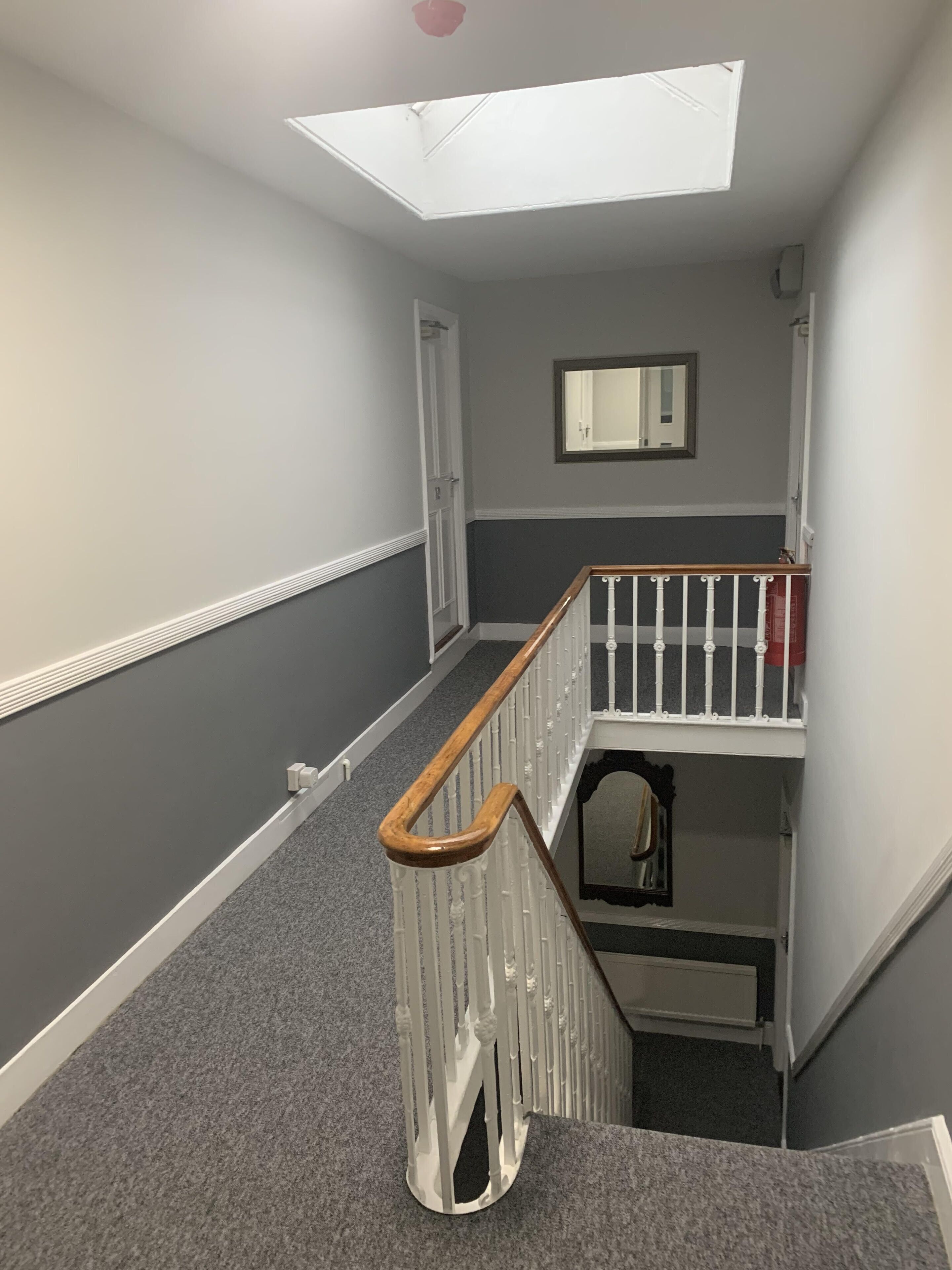 A hallway with a skylight, a white railing, and a mirror on the wall.