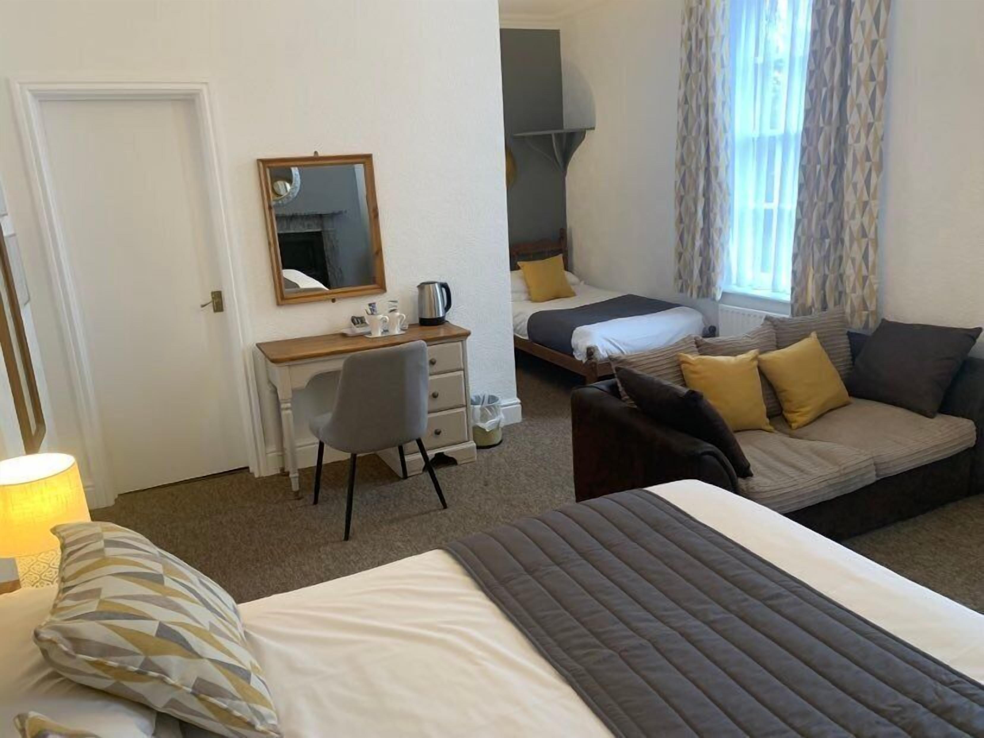 A hotel room with a bed, a sofa, a desk with a chair, a mirror, and a window with curtains.