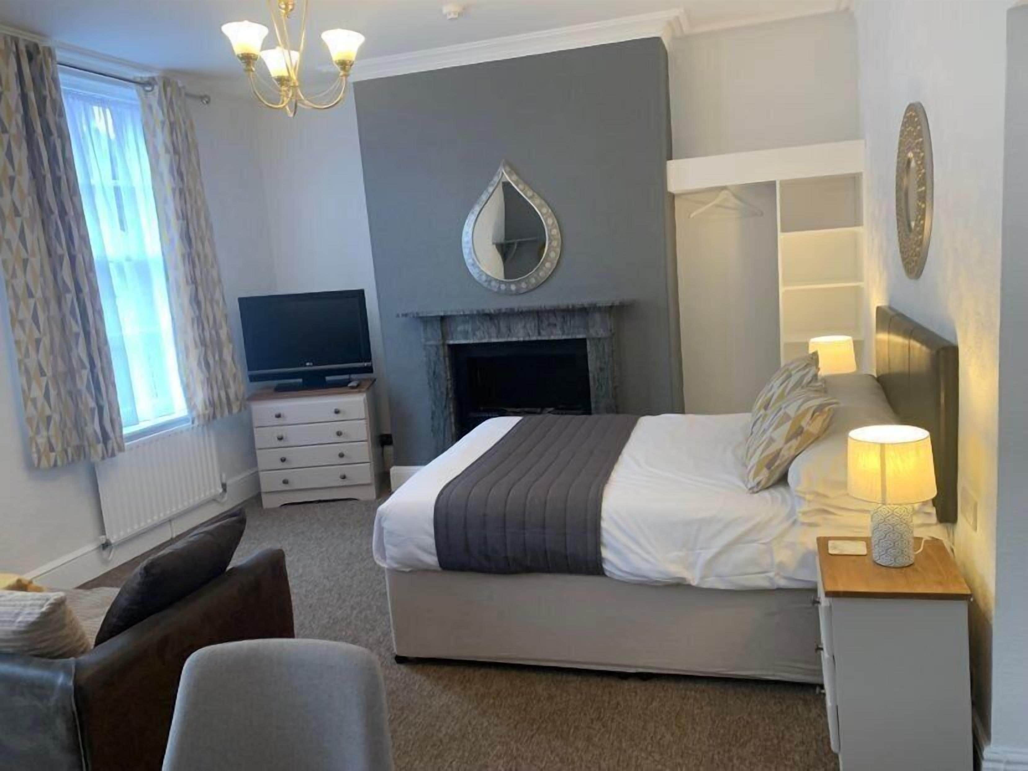 A modern bedroom with a bed, bedside lamps, a television, a fireplace, and a chandelier.