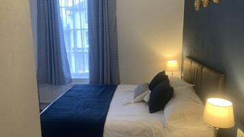 A hotel room with a bed, a bedside lamp, a window with curtains, and a wall decoration.