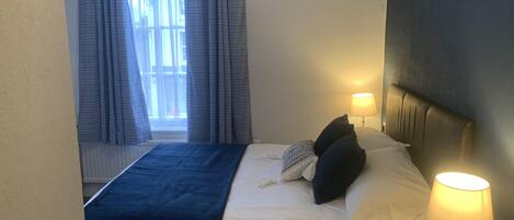 A hotel room with a bed, a bedside lamp, a window with curtains, and a wall decoration.