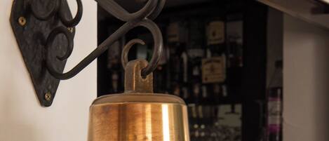 A brass bell mounted on a wall with a decorative hook.