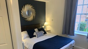 Un lit bien fait, avec une literie blanche et bleu marine, une tête de lit sombre et un élément décoratif mural.