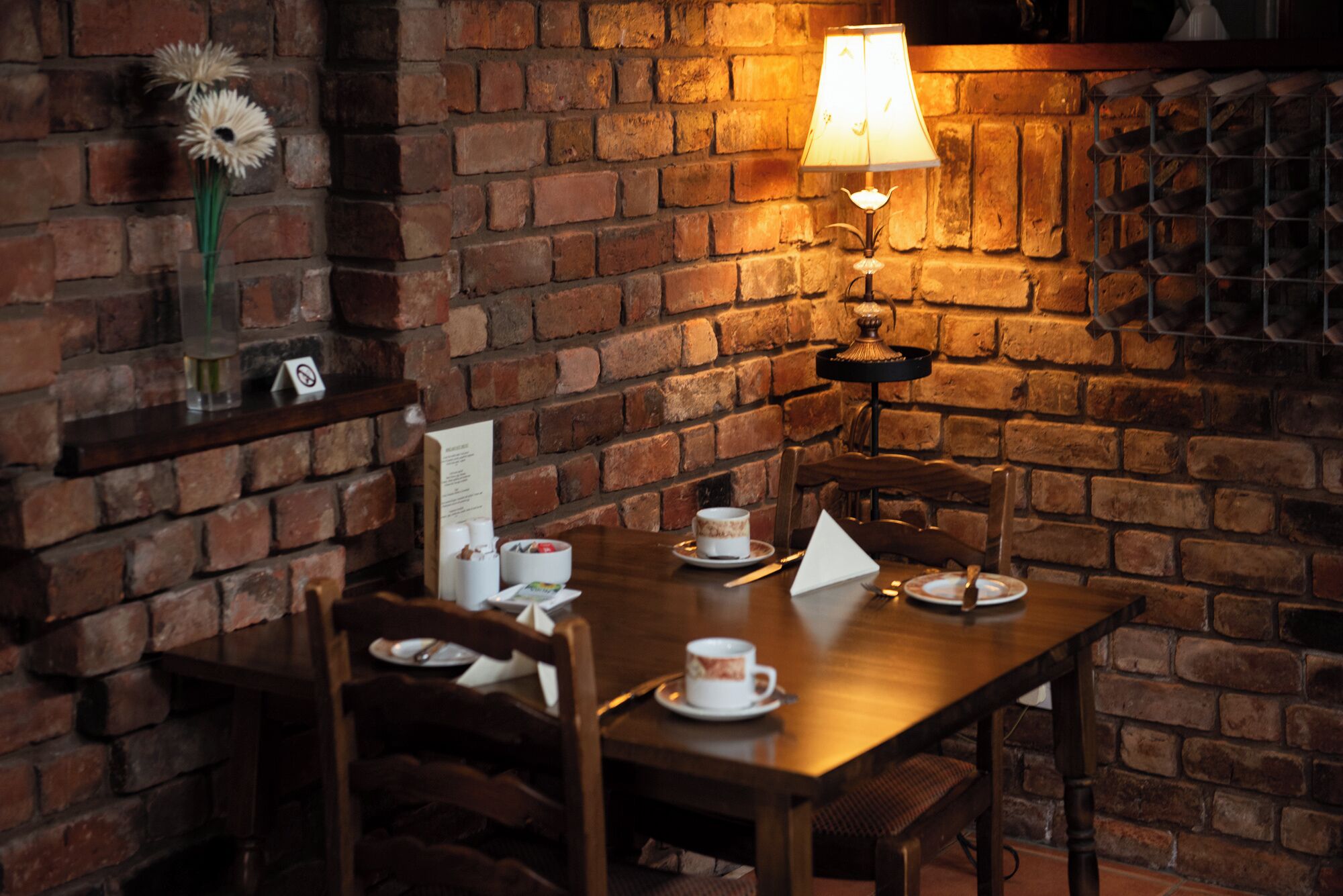 A cozy dining area with a brick wall, a table set with plates, cups, and a candle.