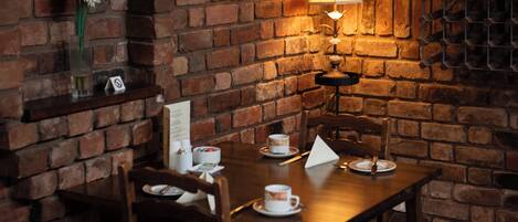 A cozy dining area with a brick wall, a table set with plates, cups, and a candle.