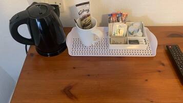 En kaffebryggare, en mugg, ett ställ för kaffekapslar och en fjärrkontroll på ett träbord.