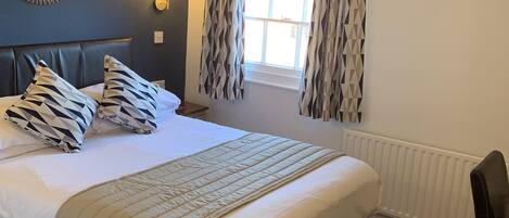 A neatly made bed with patterned pillows, a bedside lamp, and a window with curtains.