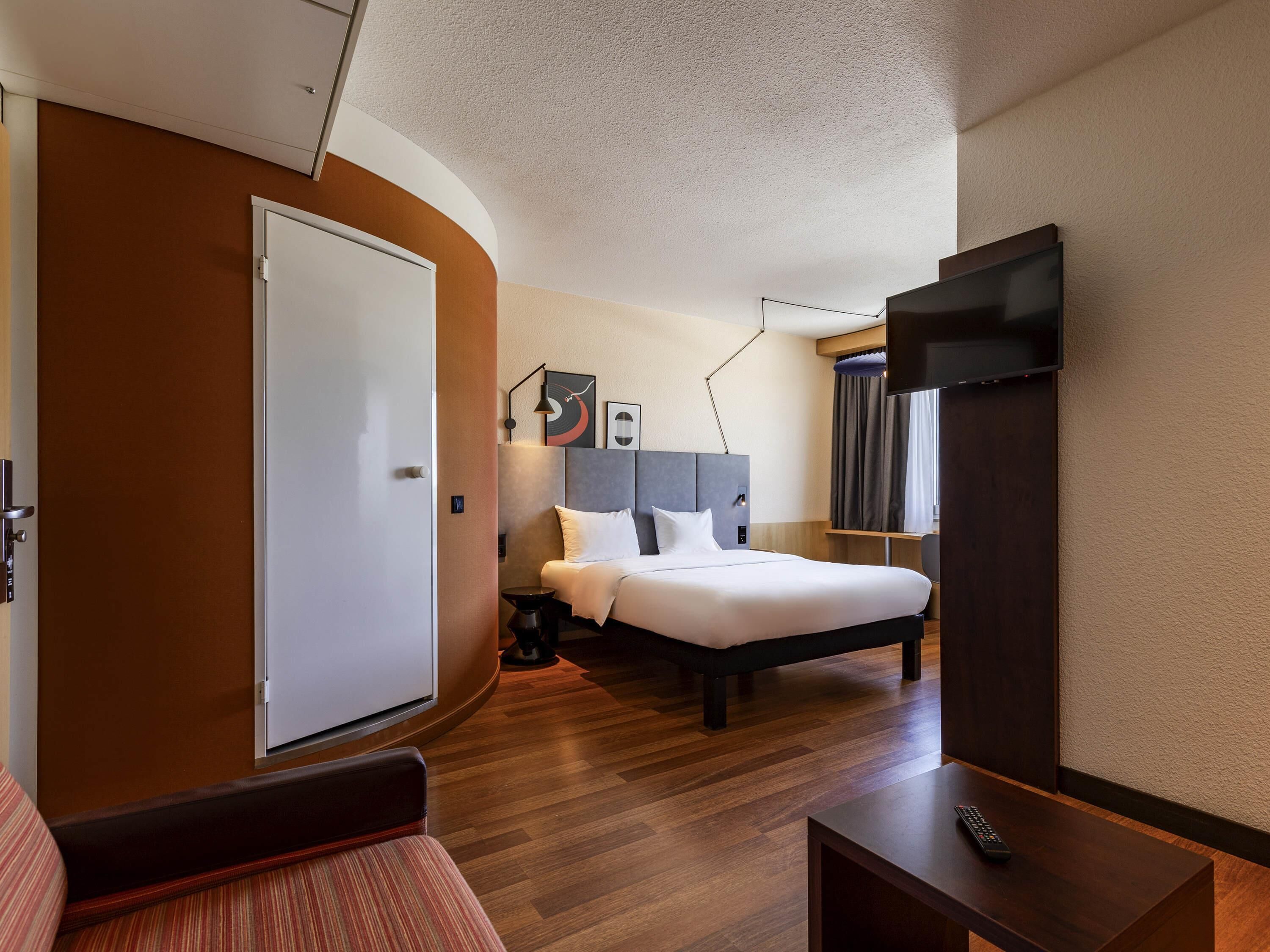 Ein Hotelzimmer mit Bett, Schreibtisch, Stuhl, Fernseher und einer Tür.