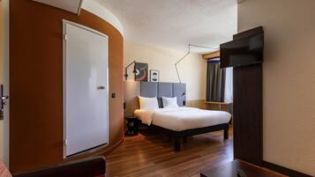 Ein Hotelzimmer mit Bett, Schreibtisch, Stuhl, Fernseher und einer Tür.