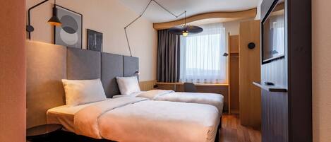 Habitación de hotel con dos camas, un escritorio, un televisor y un ventanal grande con cortinas.