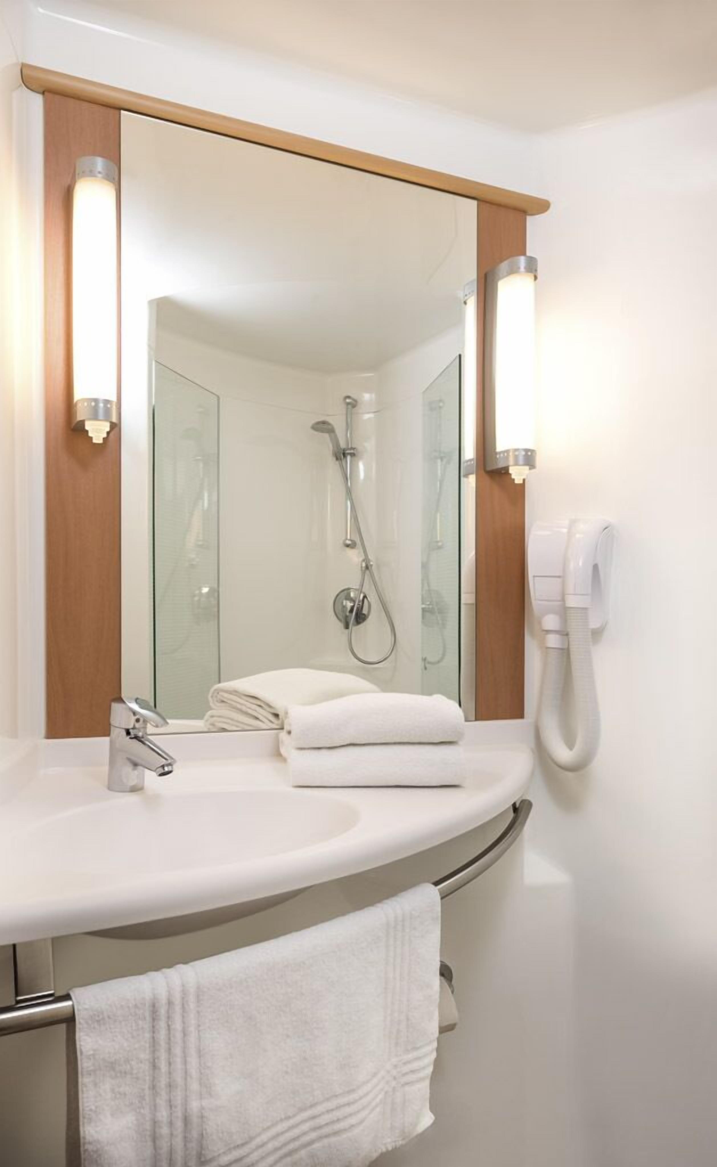 Een badkamer met een wit wastafelmeubel, een spiegel, een douche en een telefoon.