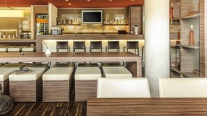 Un bar moderno con una barra larga, diversas opciones de asientos y una pantalla de televisión.