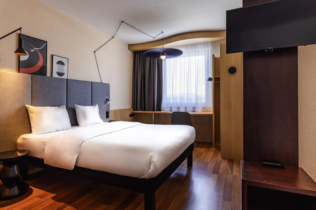Een moderne hotelkamer met een bed, nachtkastje, lamp, kunstwerk, bureau, stoel en een televisie.