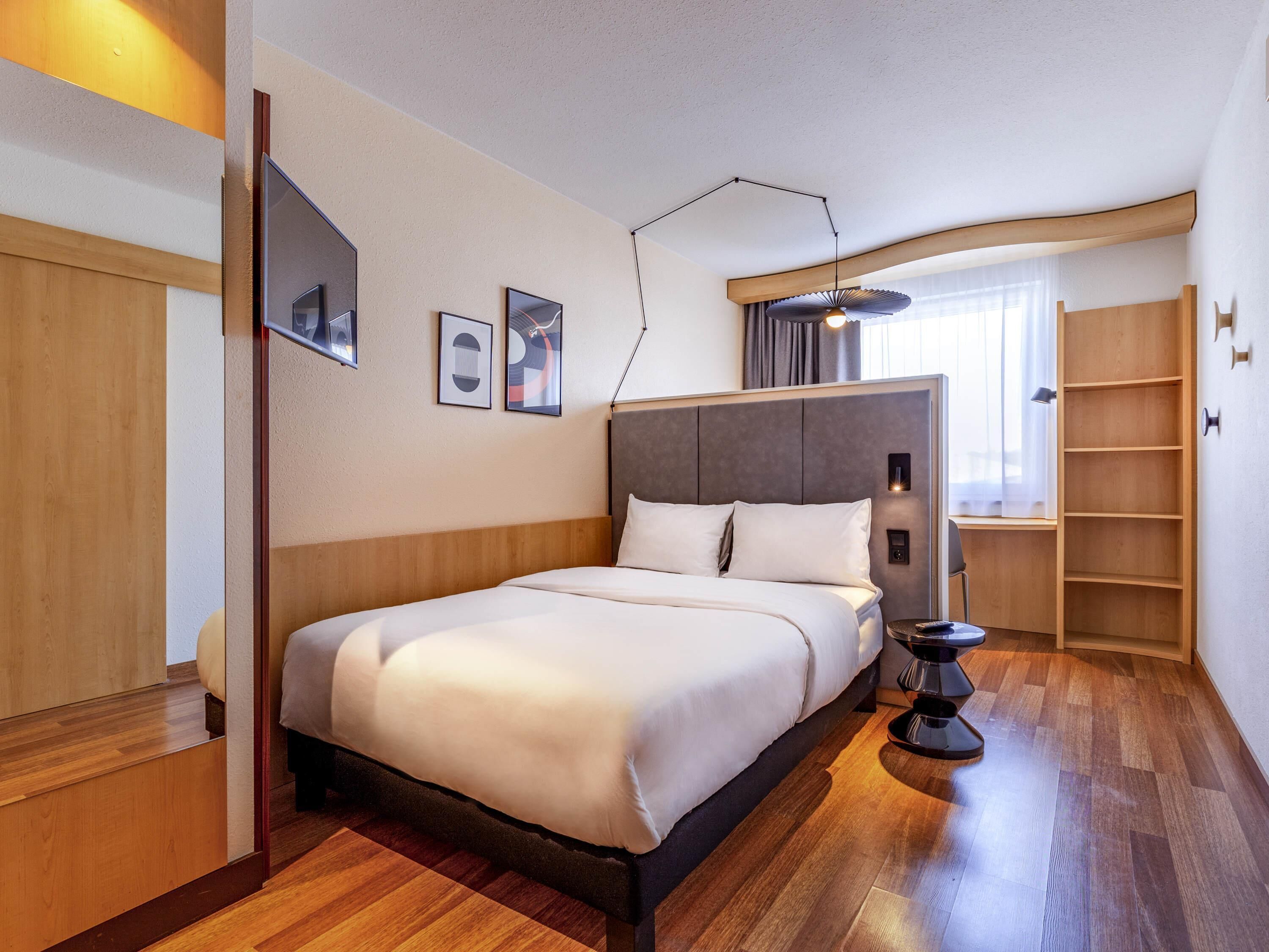 Quarto de hotel moderno com uma cama grande, mesa de cabeceira, luminária e prateleira embutida.
