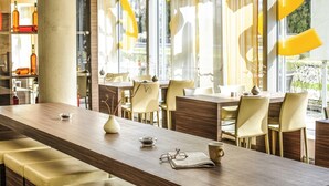 A modern dining area with a long wooden table, chairs, and a large window with curtains.