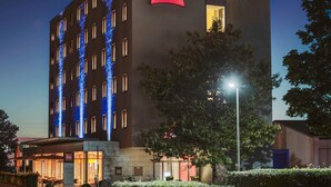 Un hotel moderno con un logotipo rojo llamativo, varios pisos y una entrada bien iluminada.