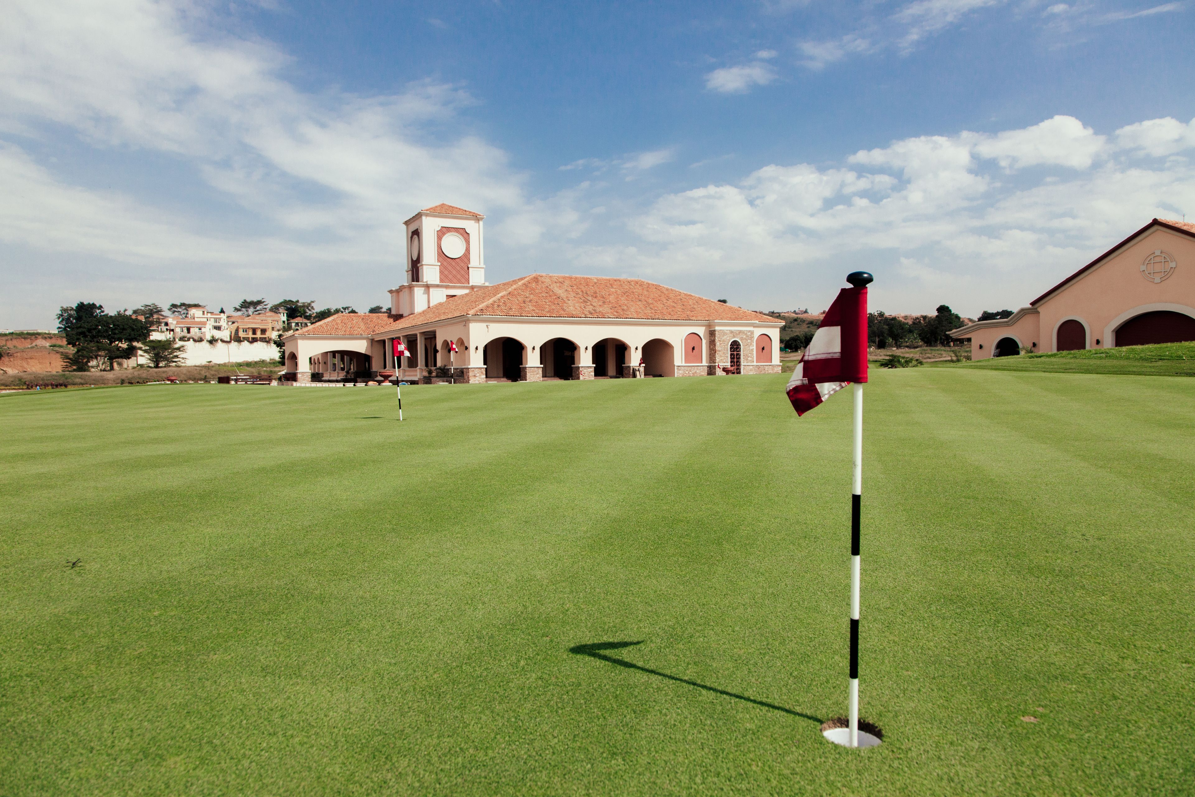 A golf course with a flagstick, a building with arches, and a clock tower in the background.