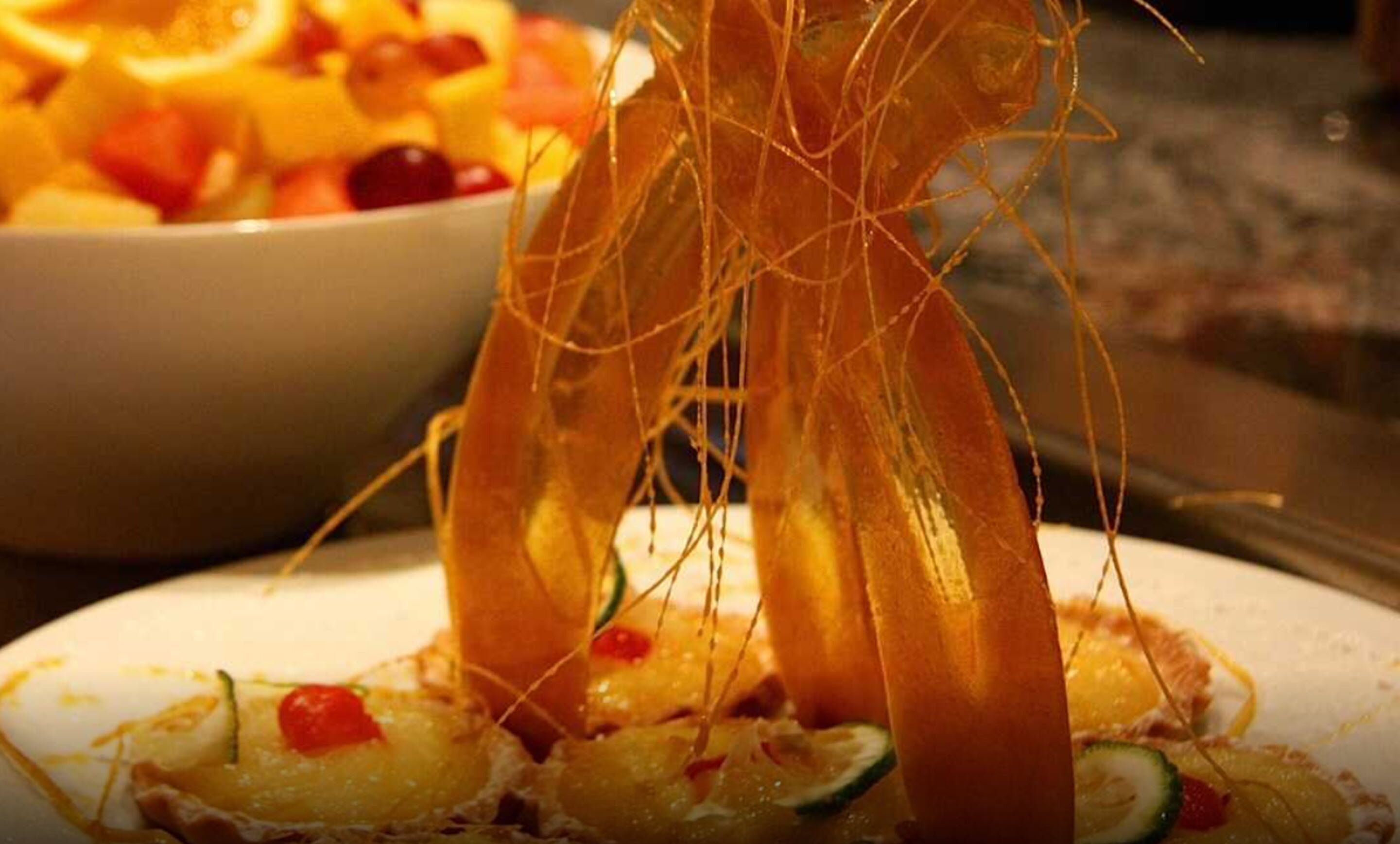 A bowl of fruit salad with visible pieces of fruit and a plate with a dish that has a garnish.