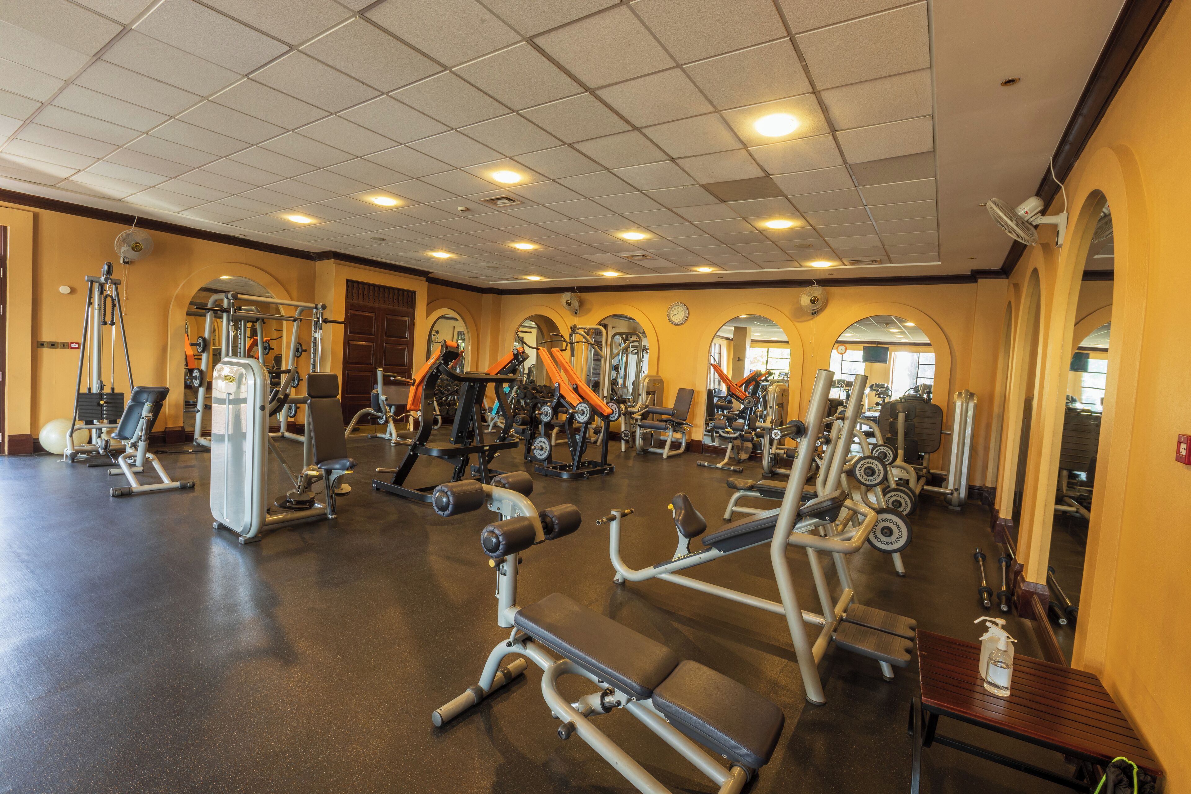 A gym with various exercise machines, mirrors, and a wooden bench.