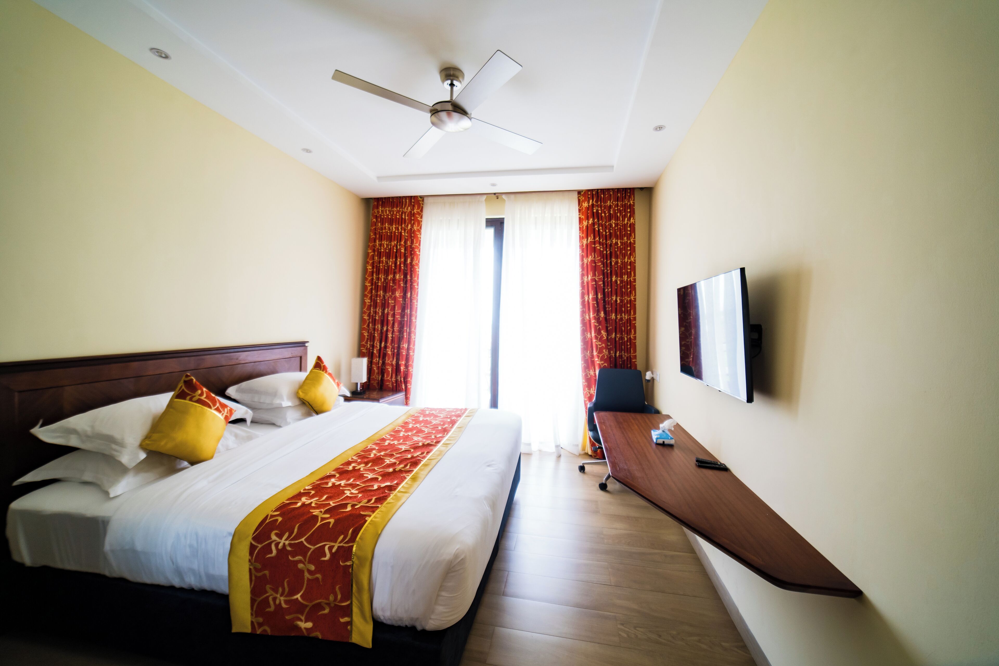 A hotel room with a bed, a desk, a chair, a TV, and a ceiling fan.