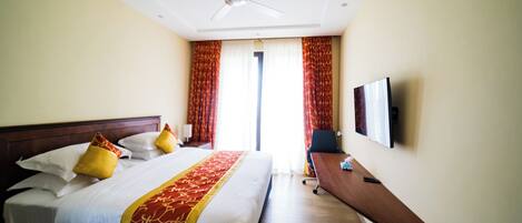 A hotel room with a bed, a desk, a chair, a TV, and a ceiling fan.