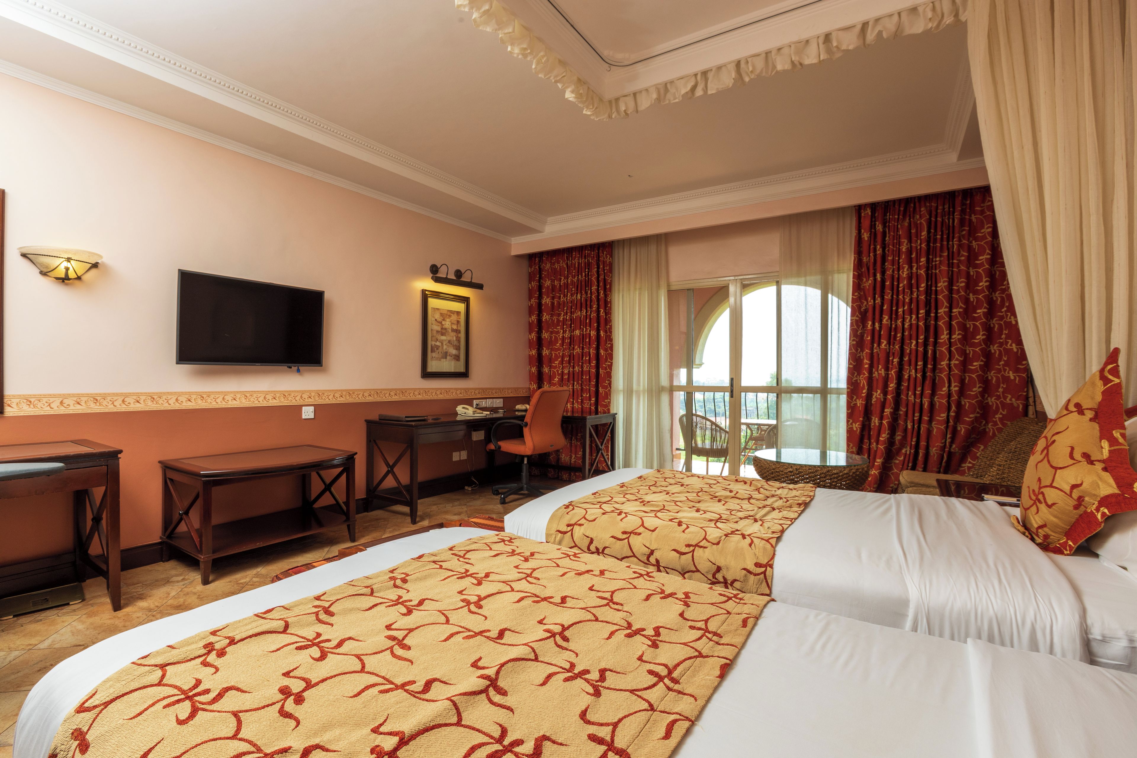 A hotel room with two beds, a desk, a chair, a television, and a window with curtains.