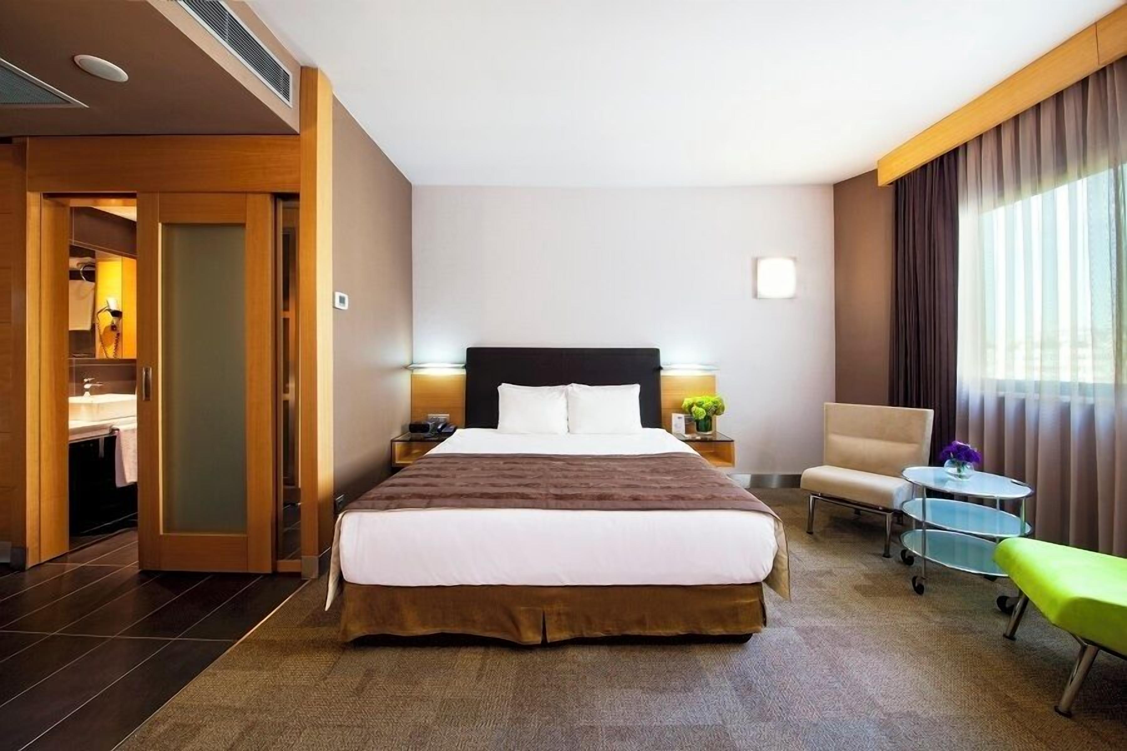 Habitación de hotel con una cama grande, mesitas de noche, una silla, una pequeña mesa y un banco.