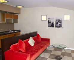 Una sala moderna con un sofá de terciopelo rojo, una mesa de centro de vidrio y una zona de cocina con armarios de madera y un lavamanos de acero inoxidable.