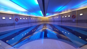 Una piscina interior moderna con iluminación azul, agua cristalina y equipo de seguridad.