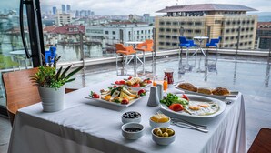 Zona de comedor en la azotea con una mesa dispuesta para el desayuno, con vistas a un paisaje urbano.