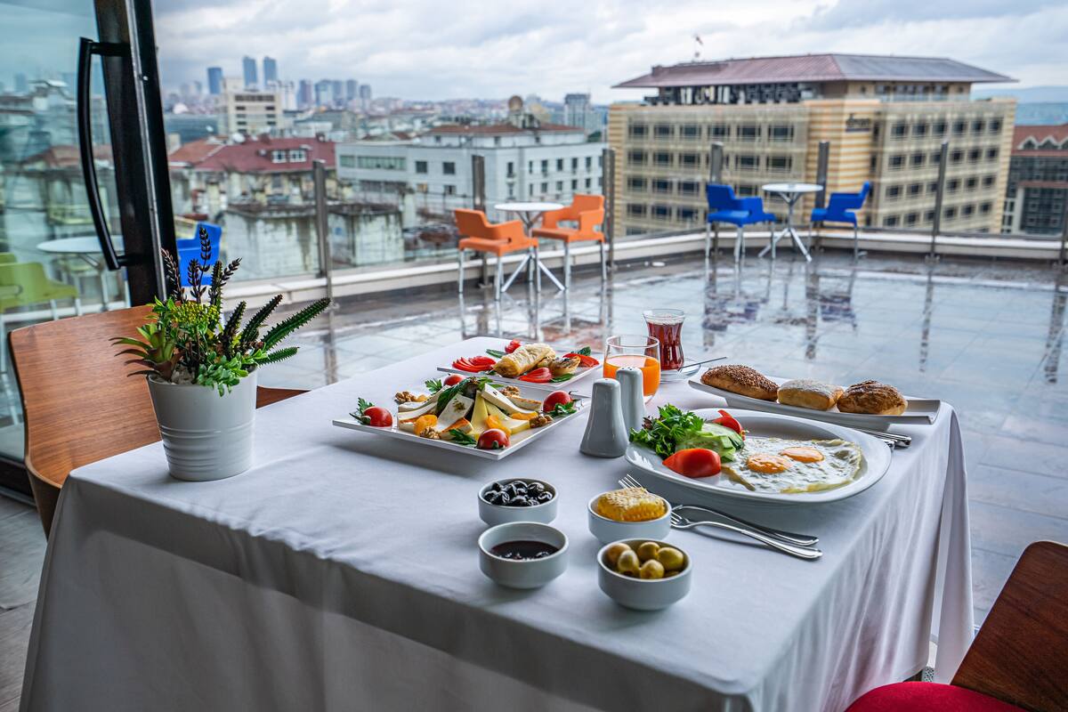 A rooftop dining area with a table set for breakfast, overlooking a cityscape.