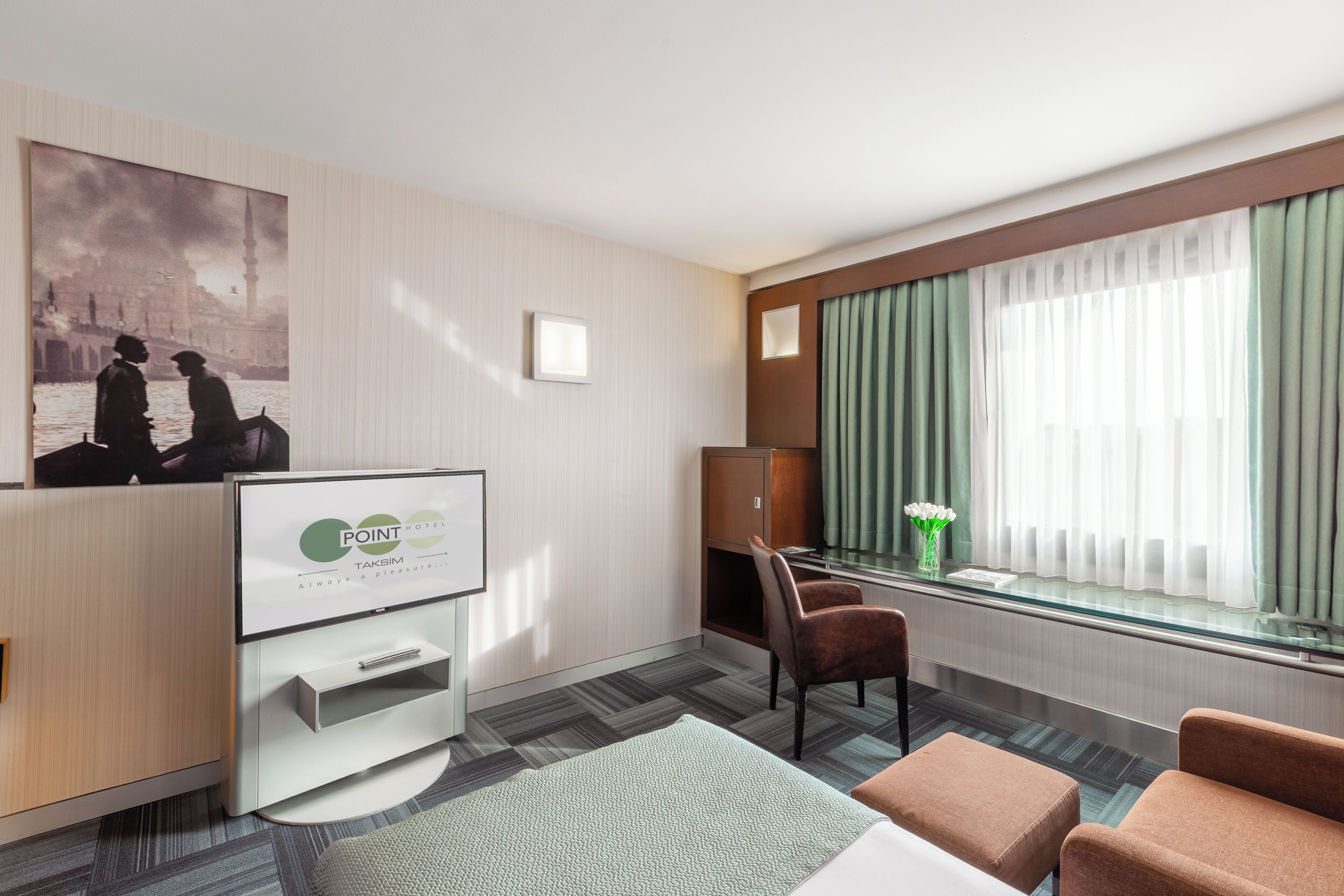 Ein Hotelzimmer mit Schreibtisch, zwei Stühlen, Fernseher, Bett und einem Fenster mit Vorhängen.
