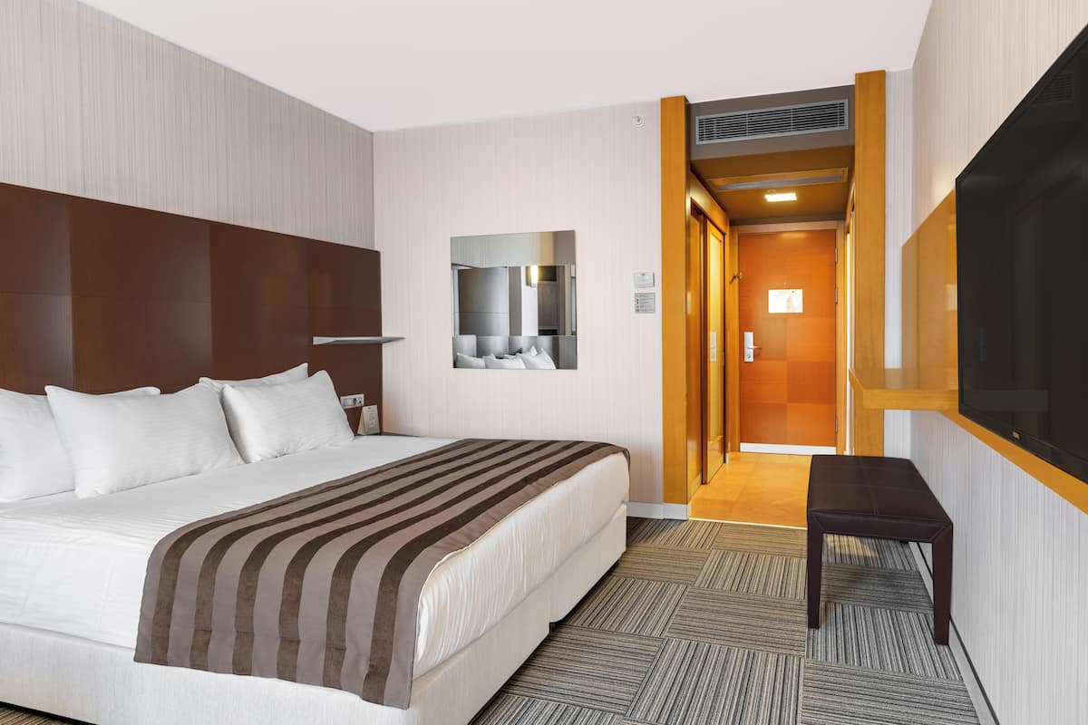 A hotel room with a large bed, a bedside table, a mirror, and a door leading to a bathroom.